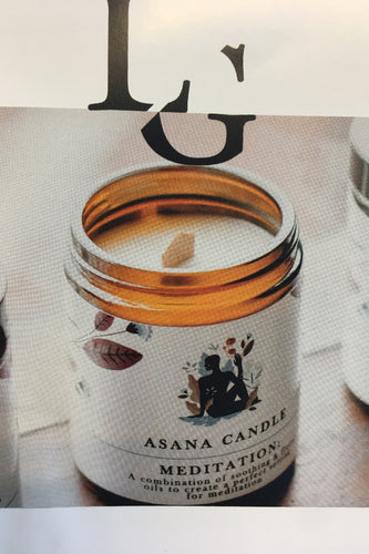 A glass jar candle with a label that reads 'Asana Candle - A Meditation Candle' along with the letter 'L' and the brand 'Light and Glo'.