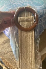 Woven belt with wooden buckle in clear packaging on a patterned fabric background