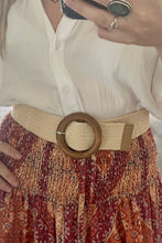 A person wearing a white shirt and a bohemian skirt with a beige woven belt featuring a faux wood round buckle.