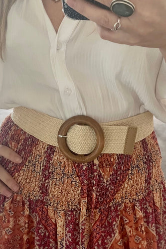 A person wearing a white shirt and a bohemian skirt with a beige woven belt featuring a faux wood round buckle.