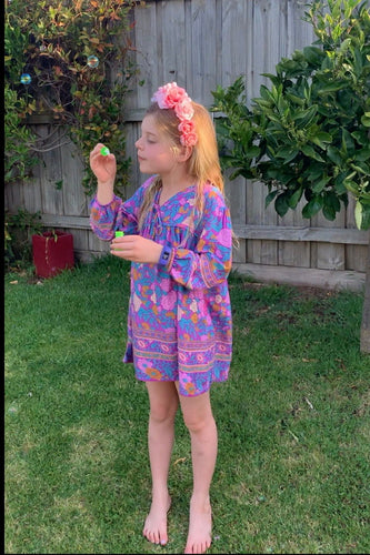 Young girl in a colorful dress playing with bubbles outdoors.