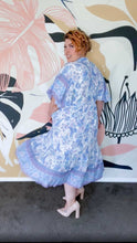 A woman wearing a blue floral boho dress, standing outside back view.
