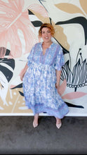 A woman wearing a blue floral boho dress, standing outside.