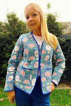Woman wearing a floral patterned jacket outdoors with greenery in the background