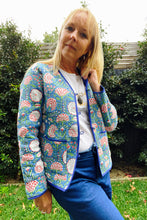 Woman wearing a floral patterned jacket outdoors with greenery in the background